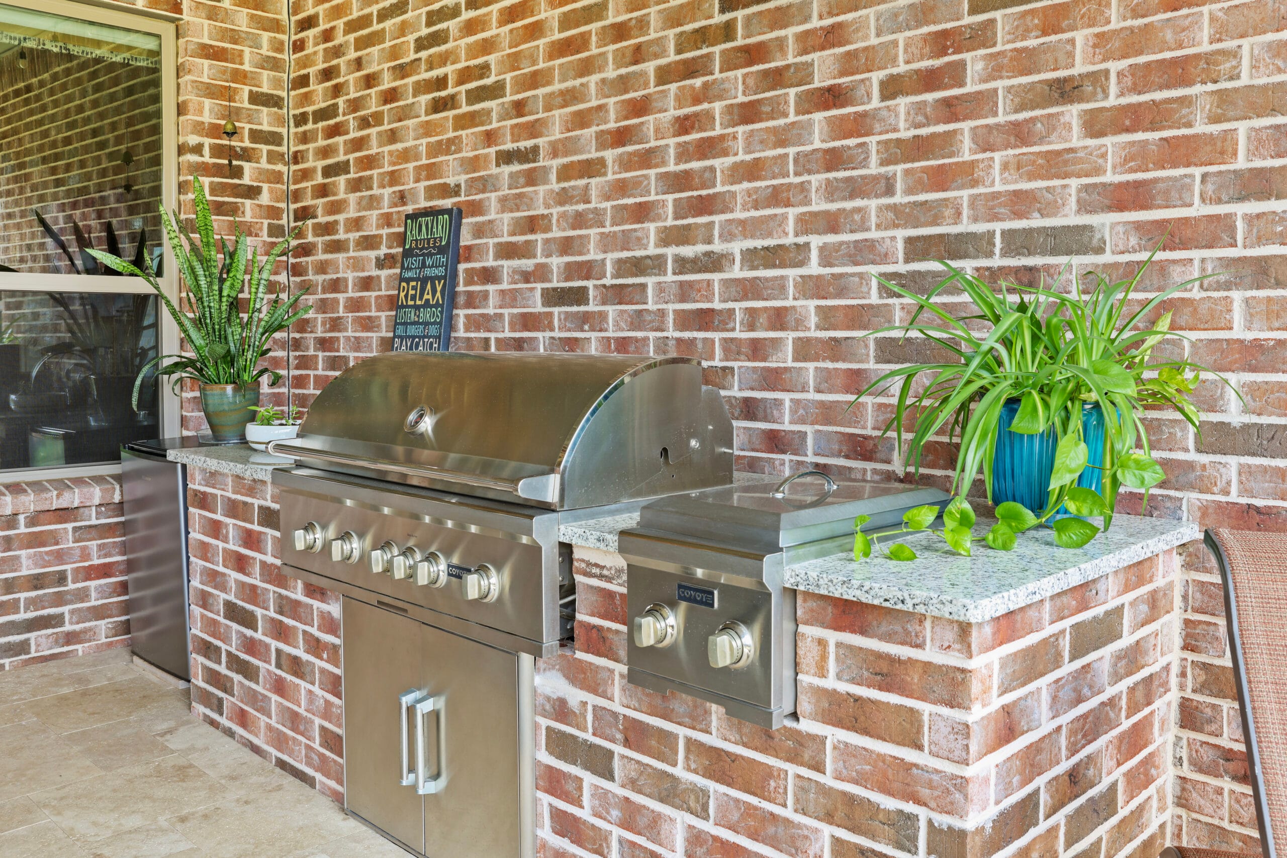 Brick outdoor kitchen with stainless steel grill beneath a covered patio