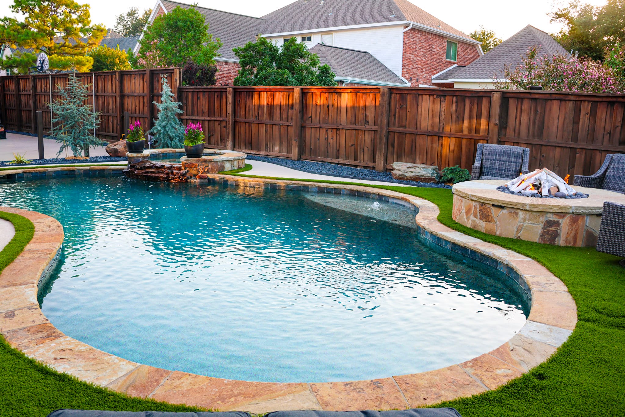 Remodeled backyard pool with raised spa, fire pit, turf, and seating in Coppell