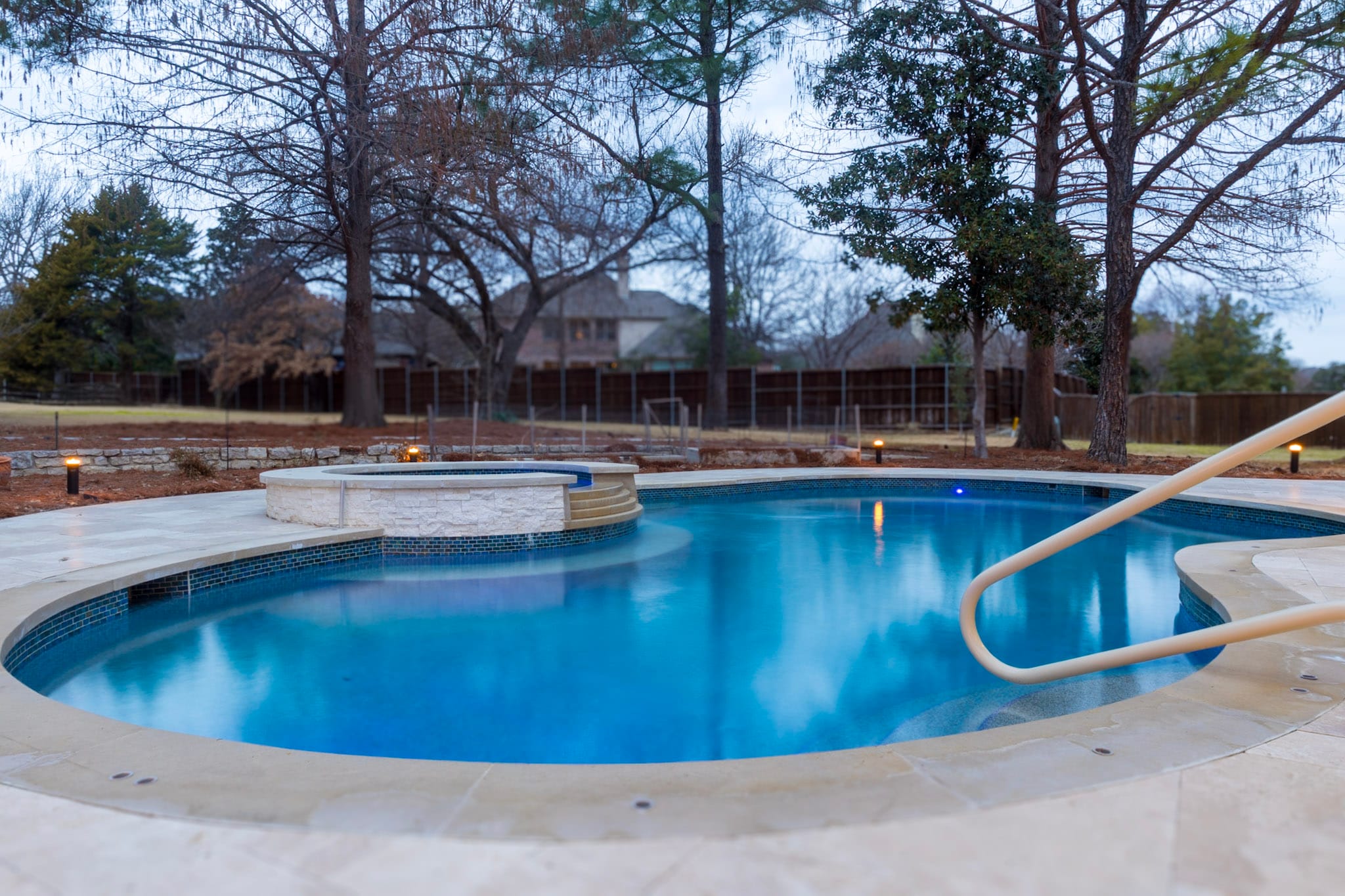 Curved swimming pool with raised spa and entry handrail at twilight