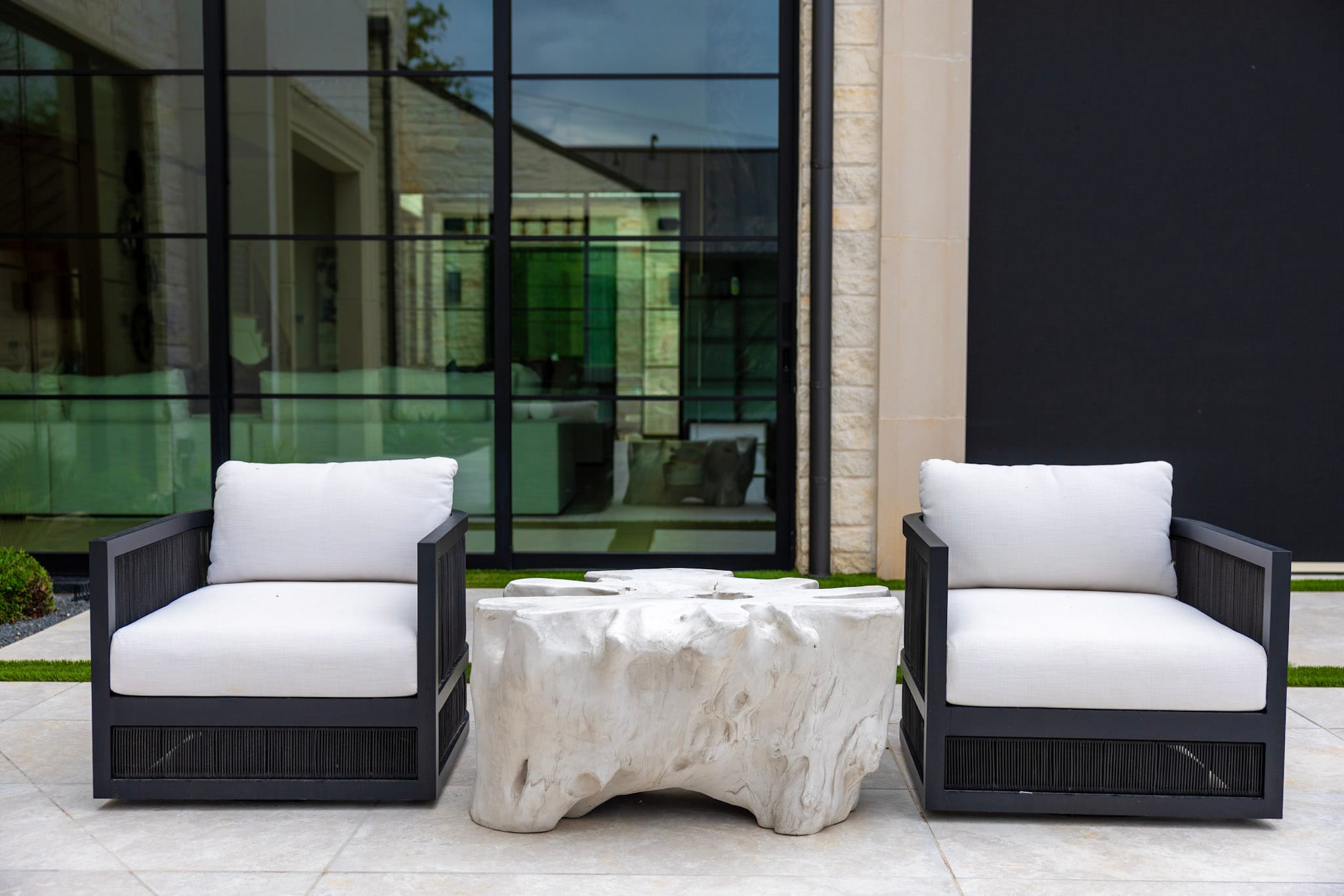 Two black lounge chairs with white cushions beside sculptural outdoor table