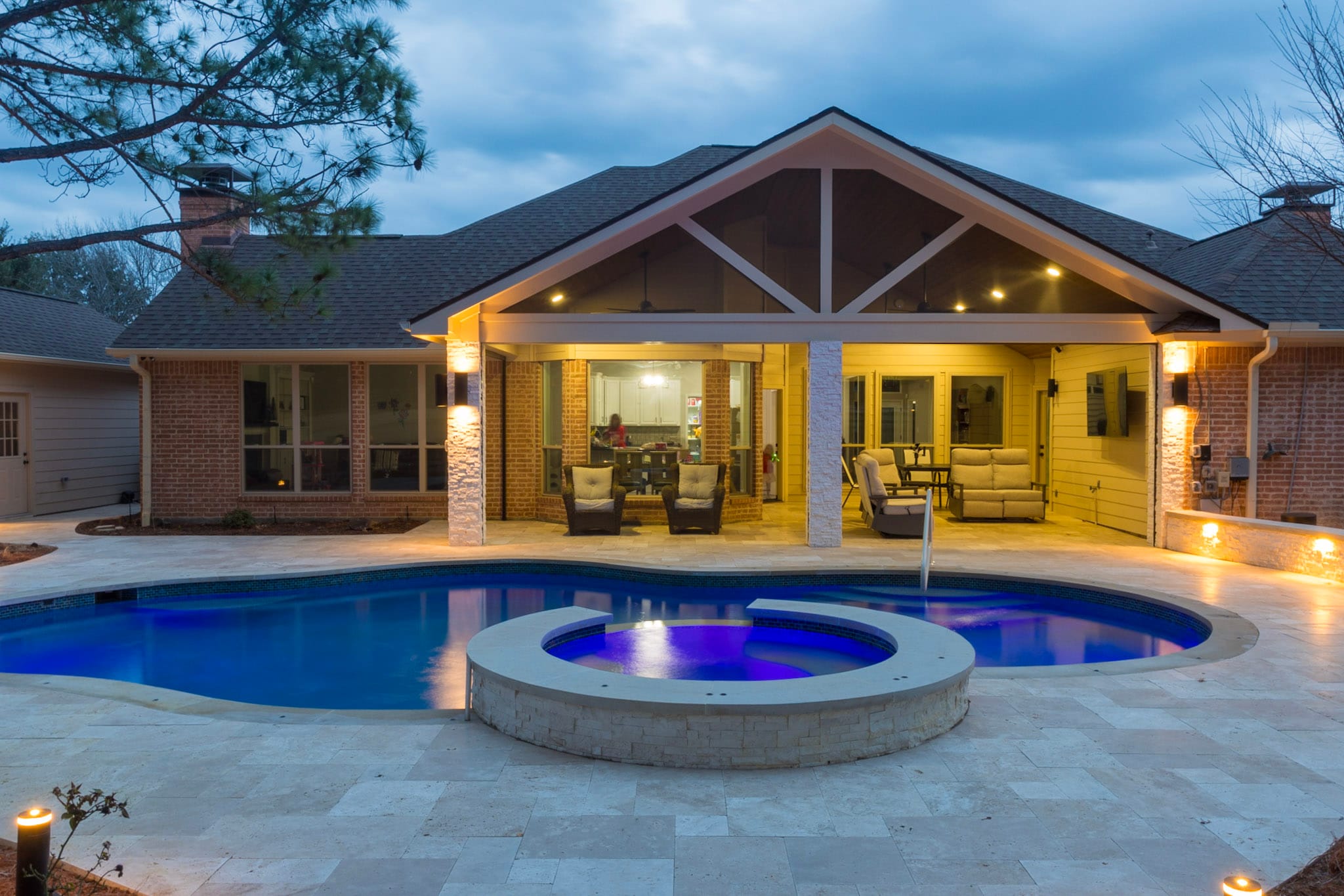 Blue illuminated pool and raised spa facing a lighted covered patio