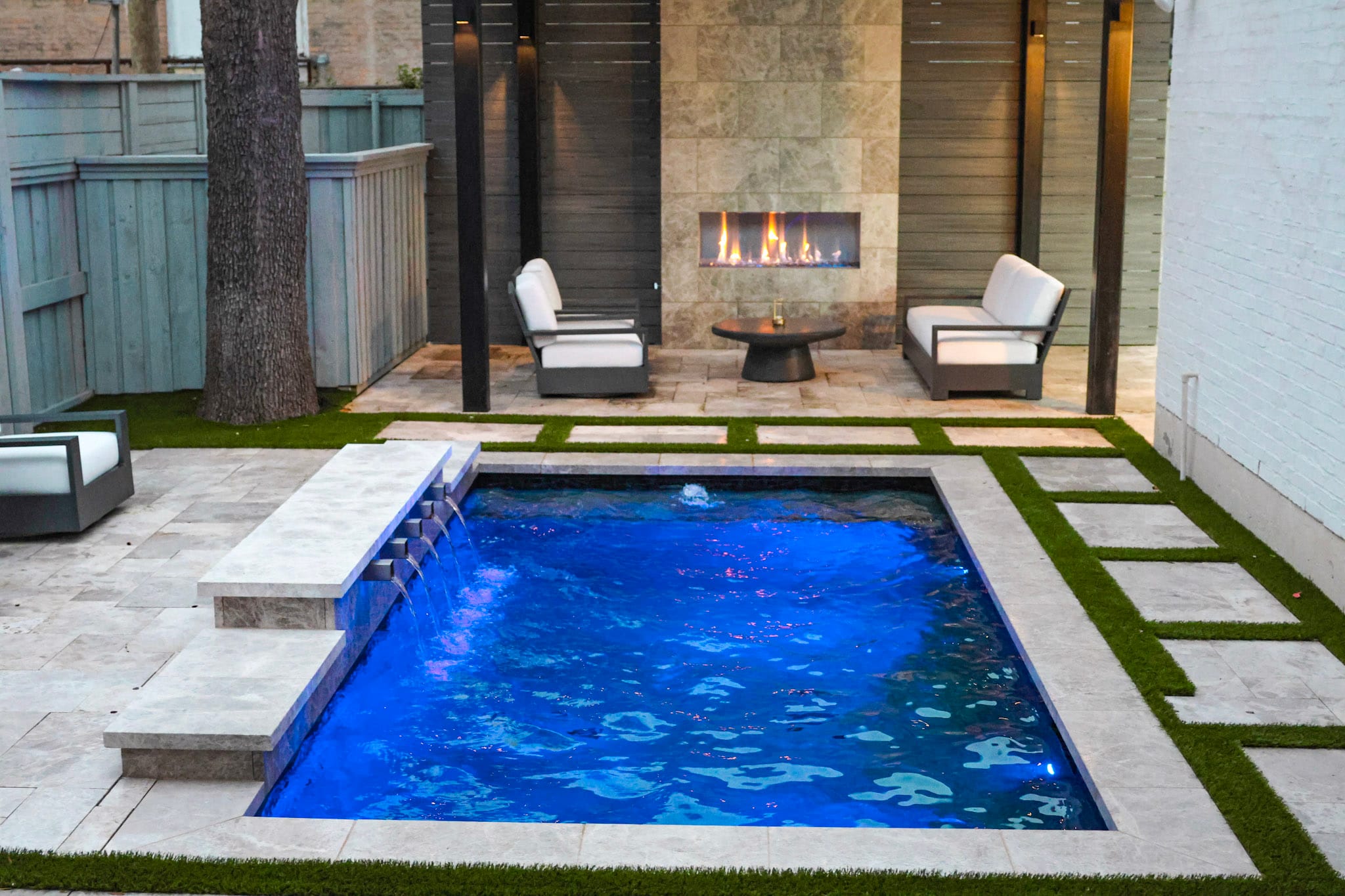 Blue-lit cocktail pool facing covered patio with linear fireplace