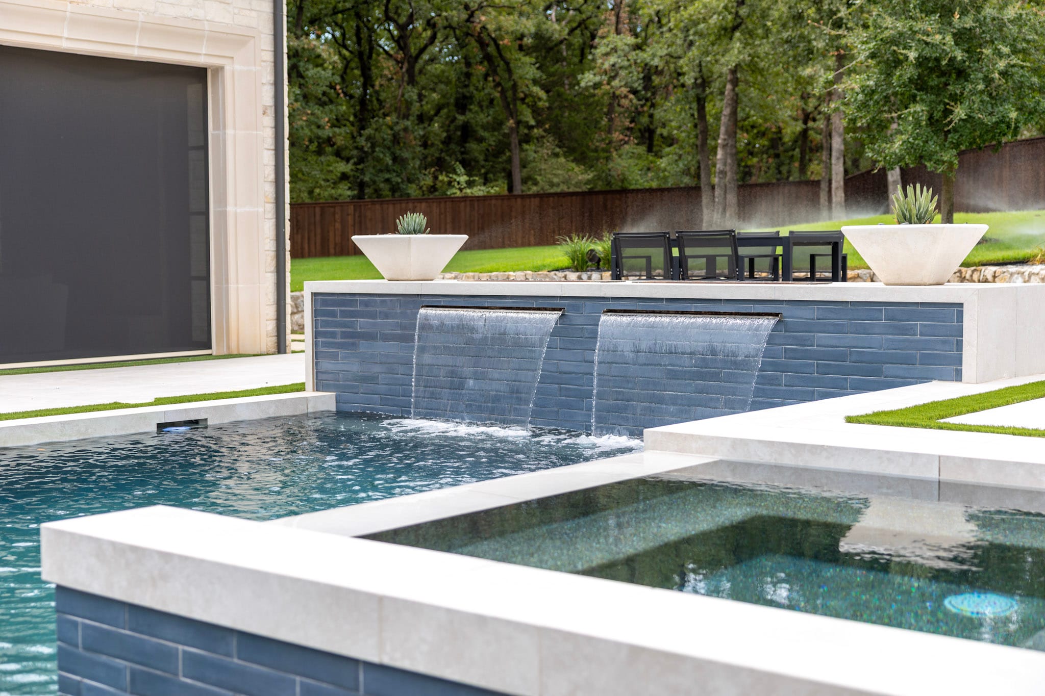 Raised spa beside pool with two sheet waterfalls in background