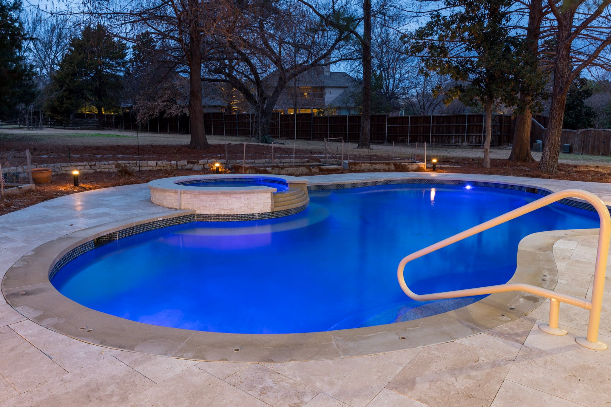 Freeform pool glowing blue beside a raised spa at dusk