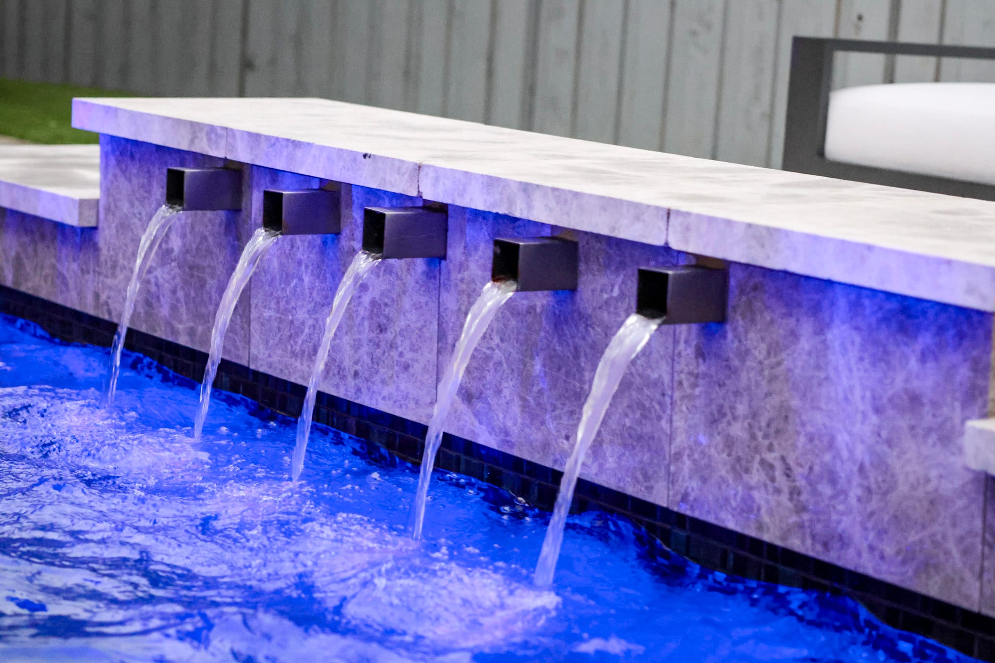 Five square scuppers flowing into a blue-lit swimming pool