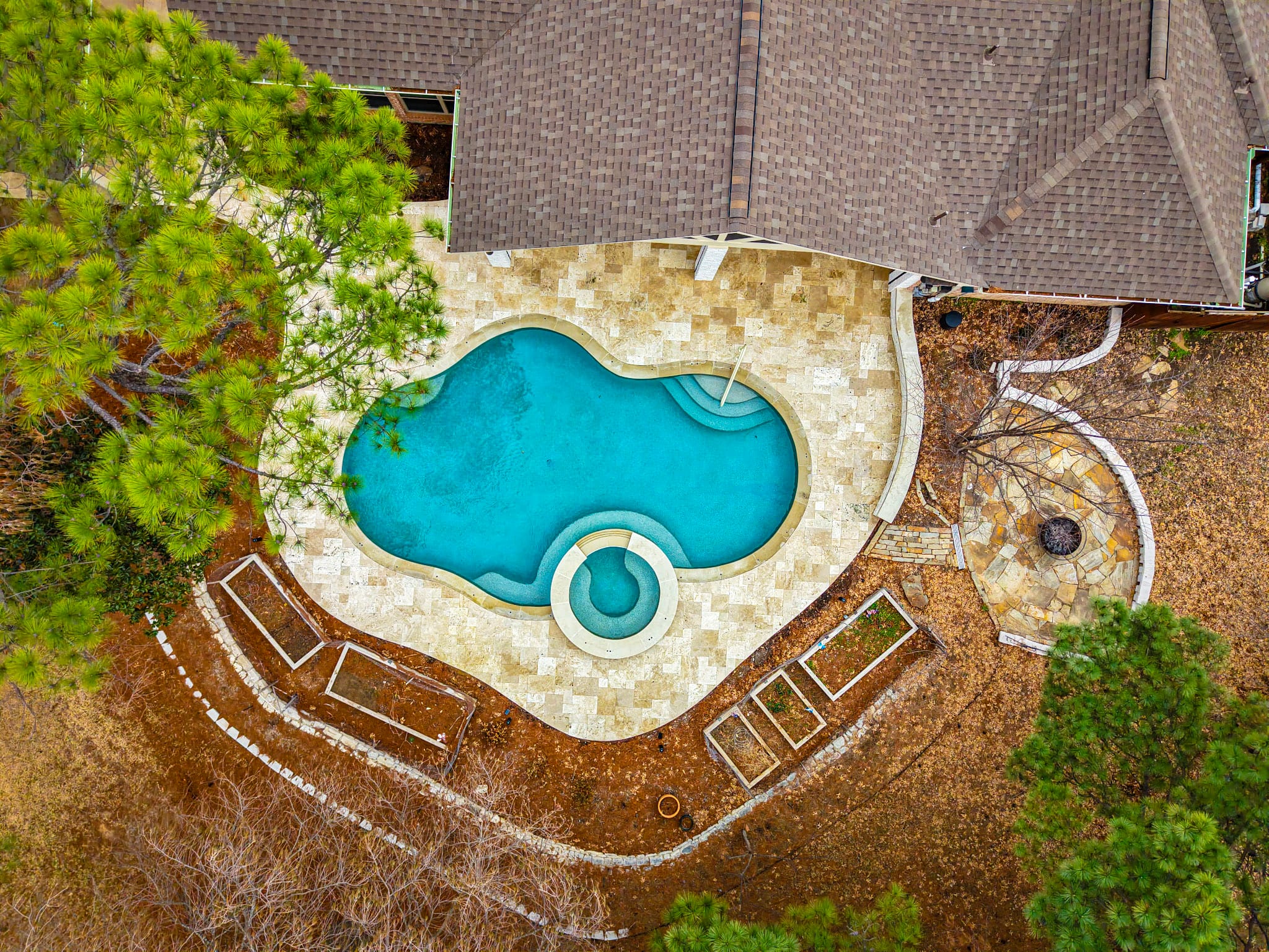 Overhead drone view of a freeform pool, circular spa, and travertine deck