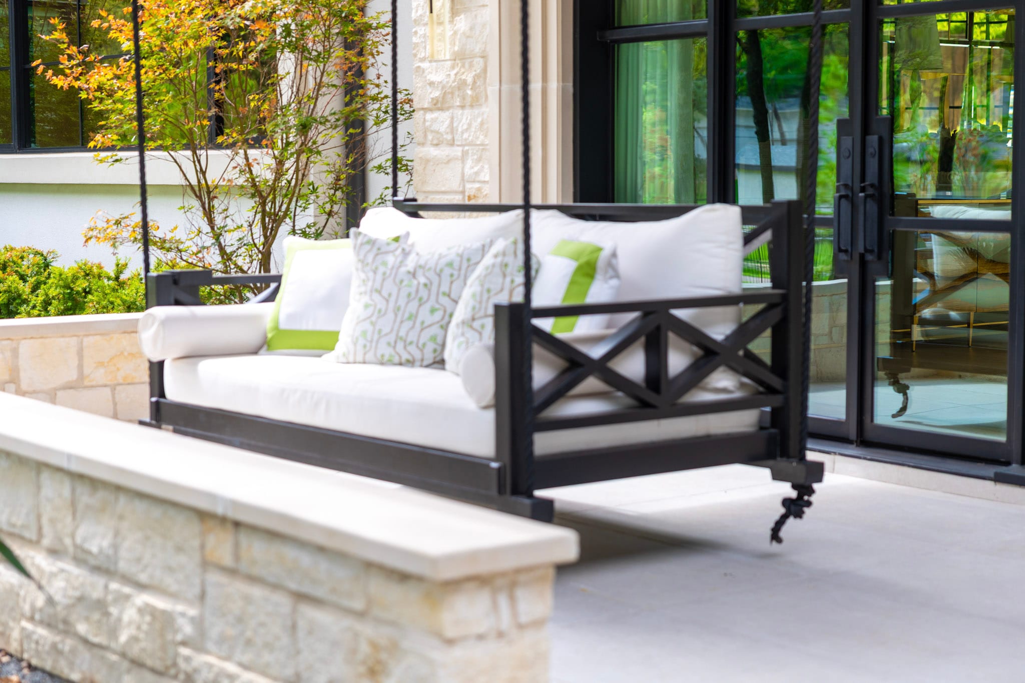 Black suspended porch swing with white cushions beside glass doors