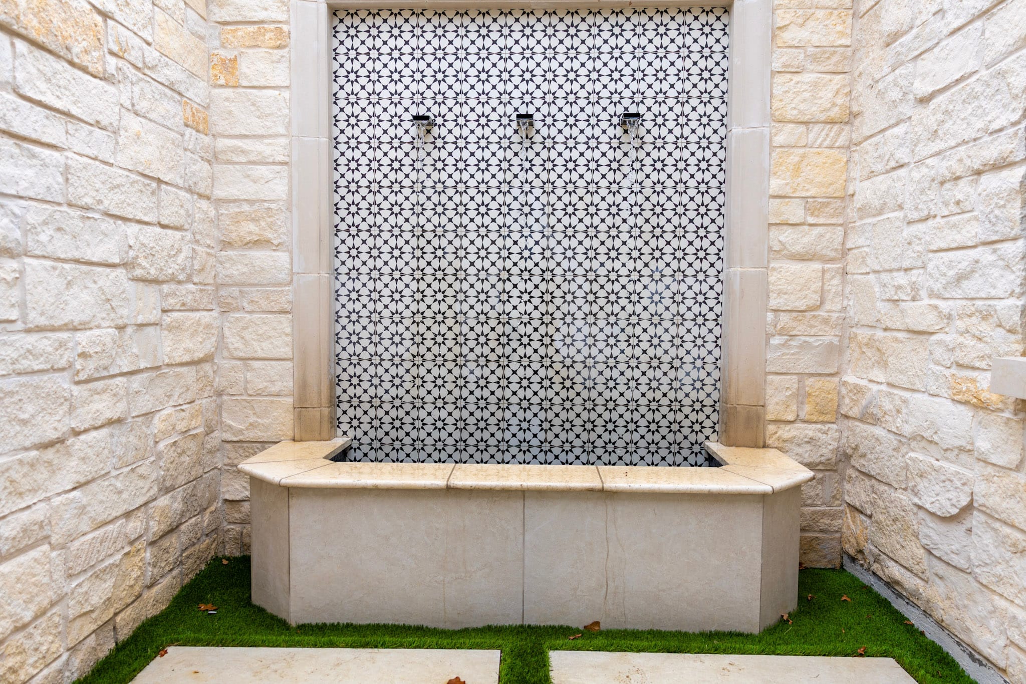 Patterned tiled fountain wall surrounded by light stone walls