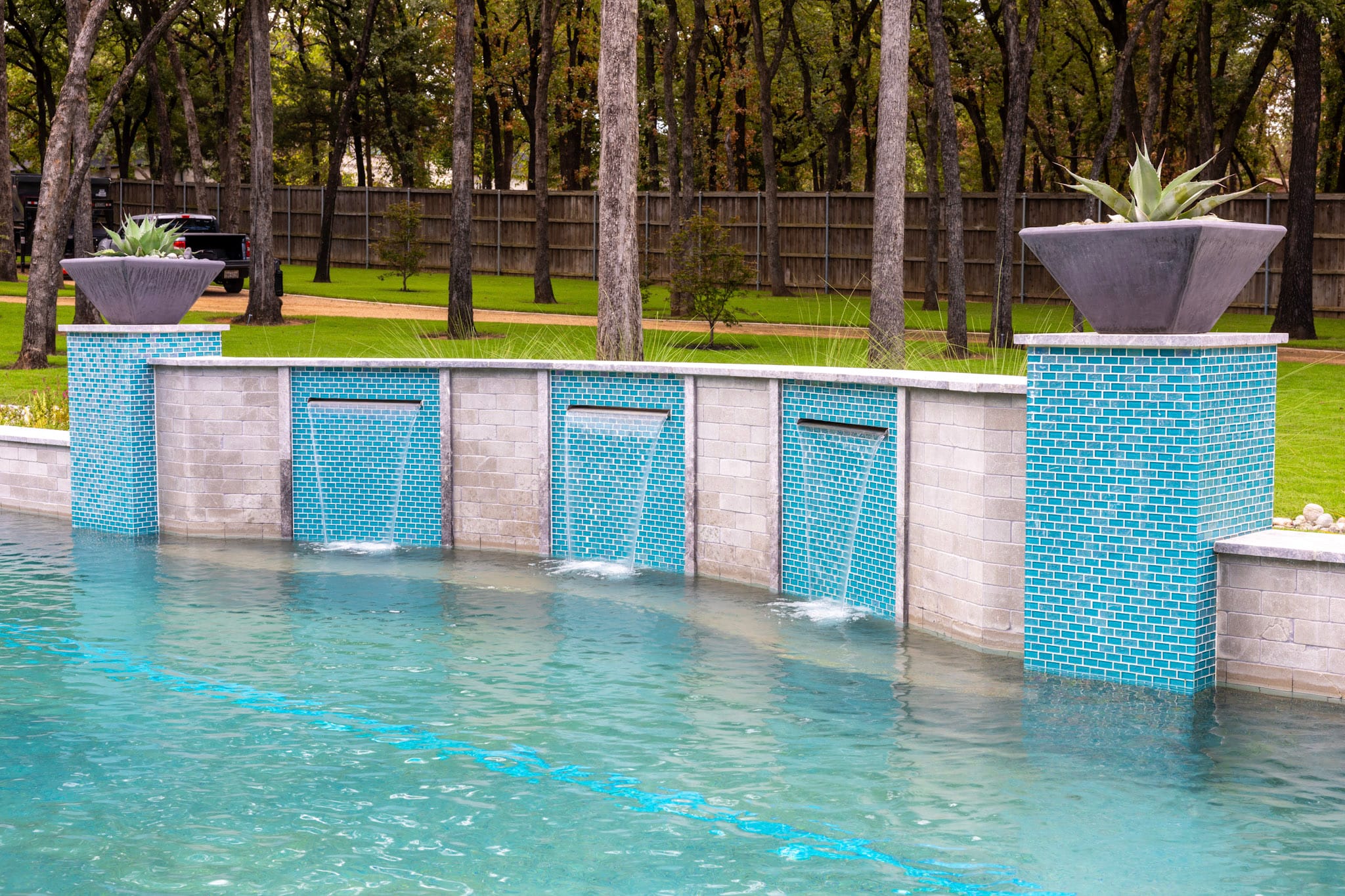 Three pool waterfalls flowing from curved turquoise tile and stone feature wall in Southlake