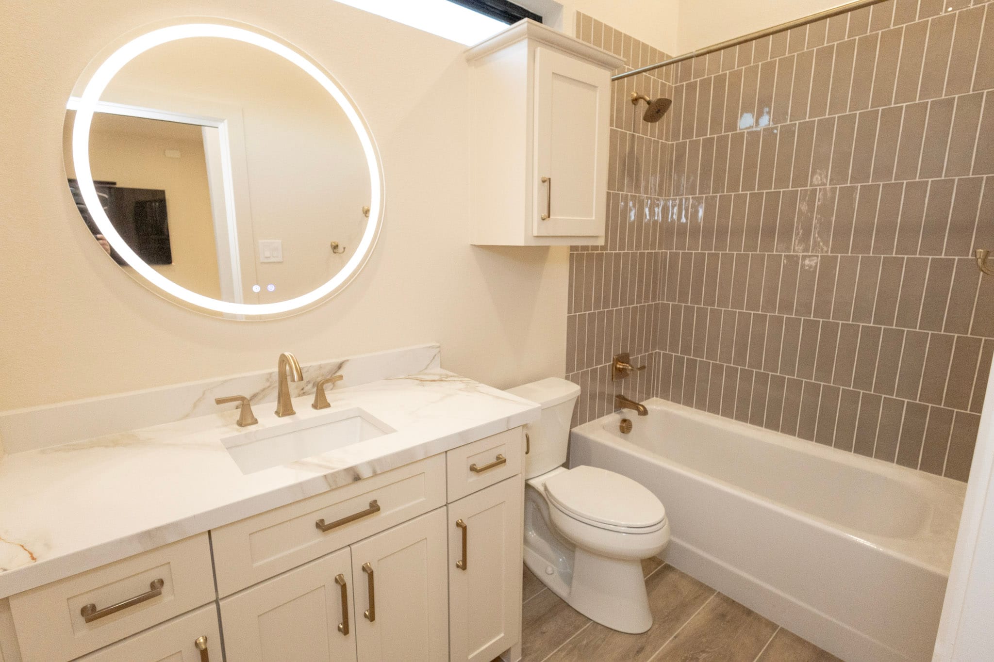 Bathroom with illuminated round mirror, white vanity, and tiled tub surround