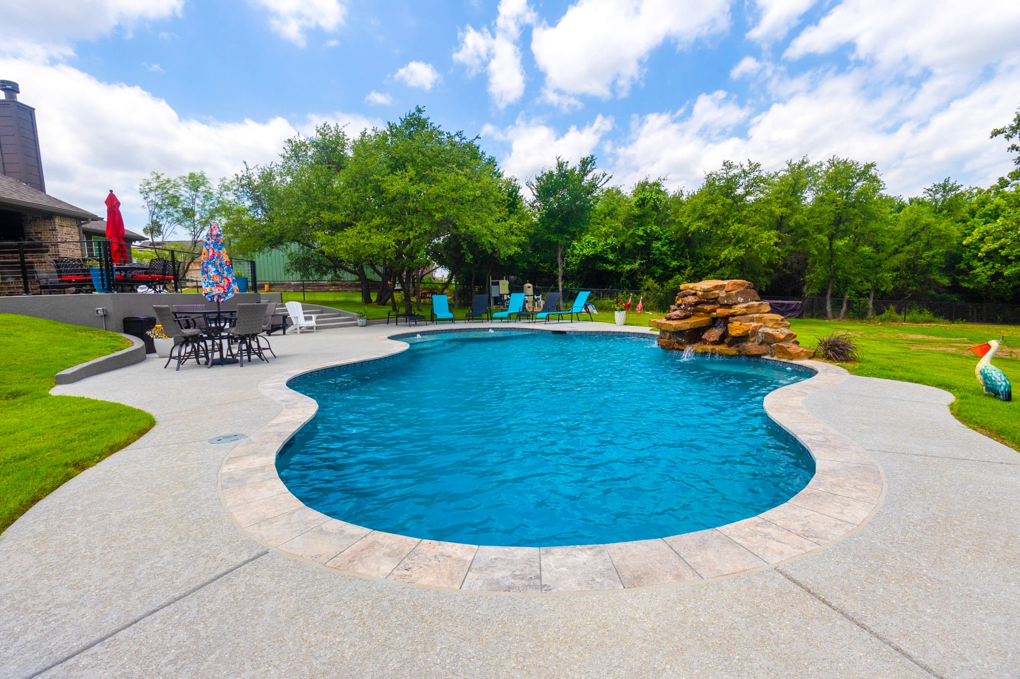 Freeform backyard pool with rock waterfall and surrounding patio in Weatherford