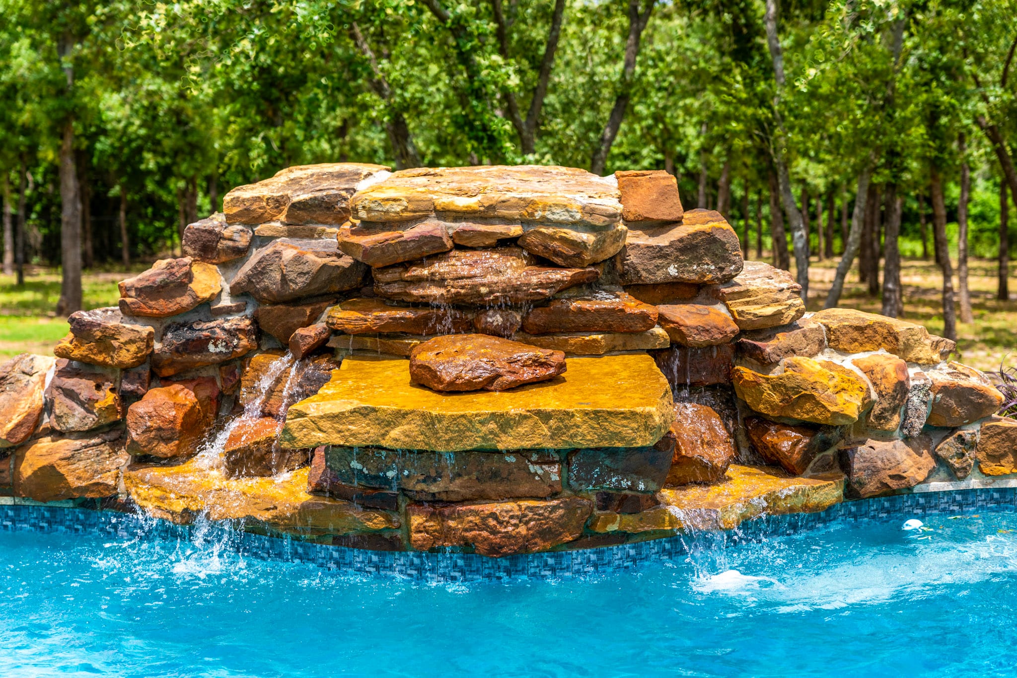 Close view of stacked rock waterfall flowing into blue swimming pool