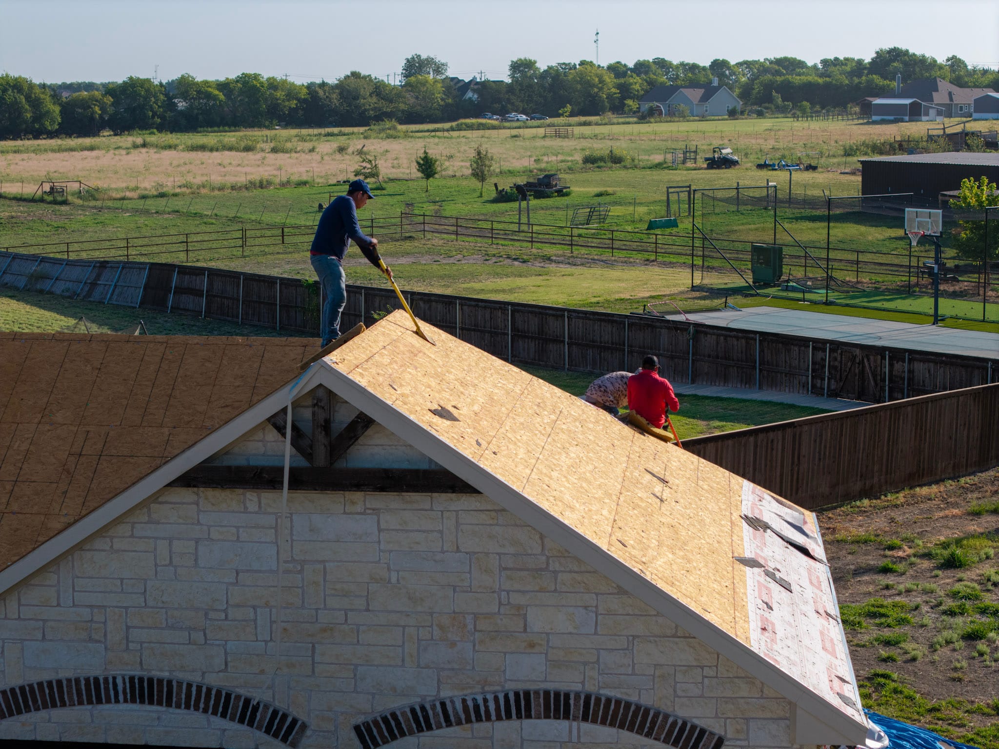 Drone view of large residential roofing project with workers and blue tarps