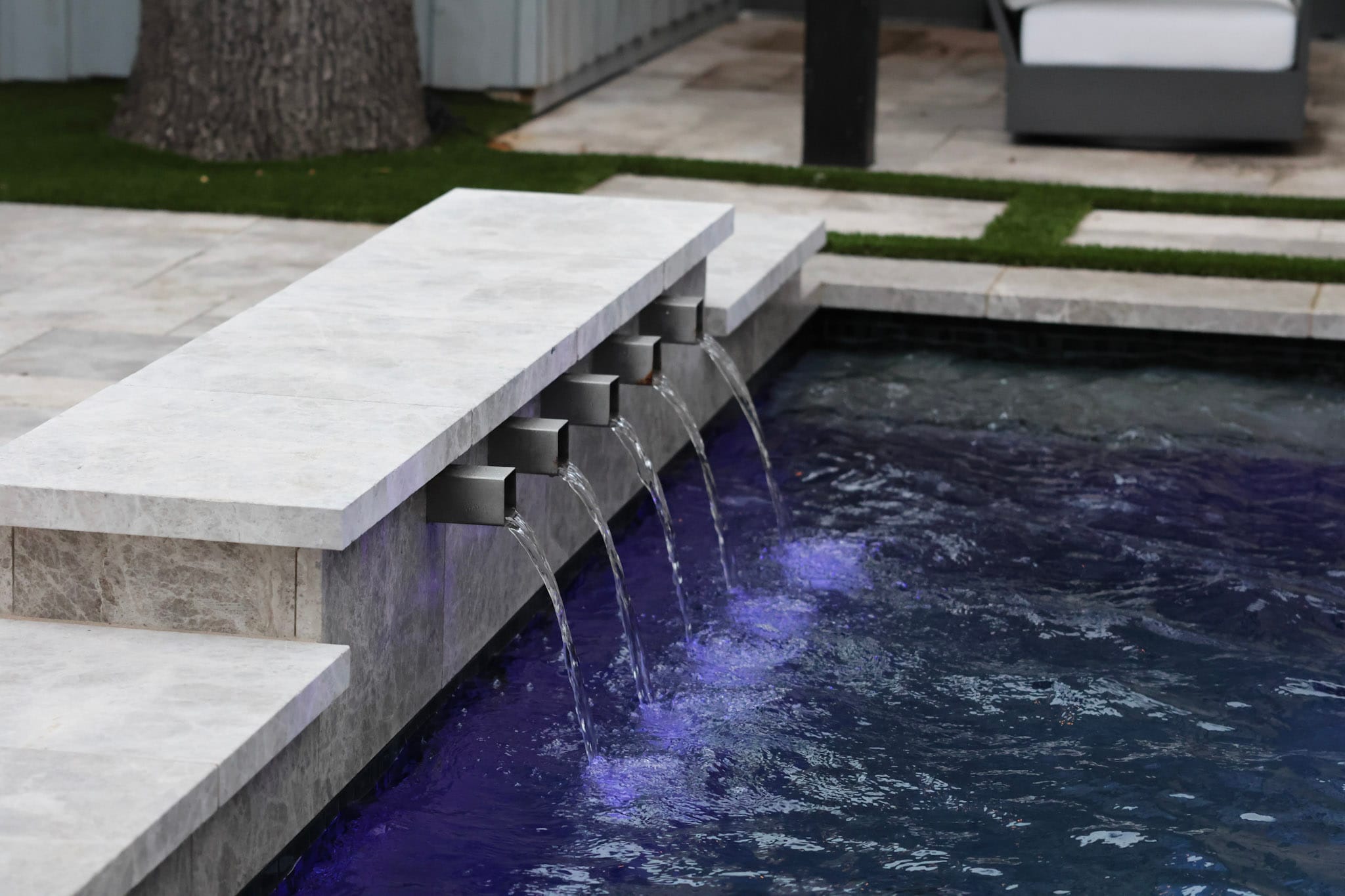 Raised pool wall with five scuppers and patio seating beyond