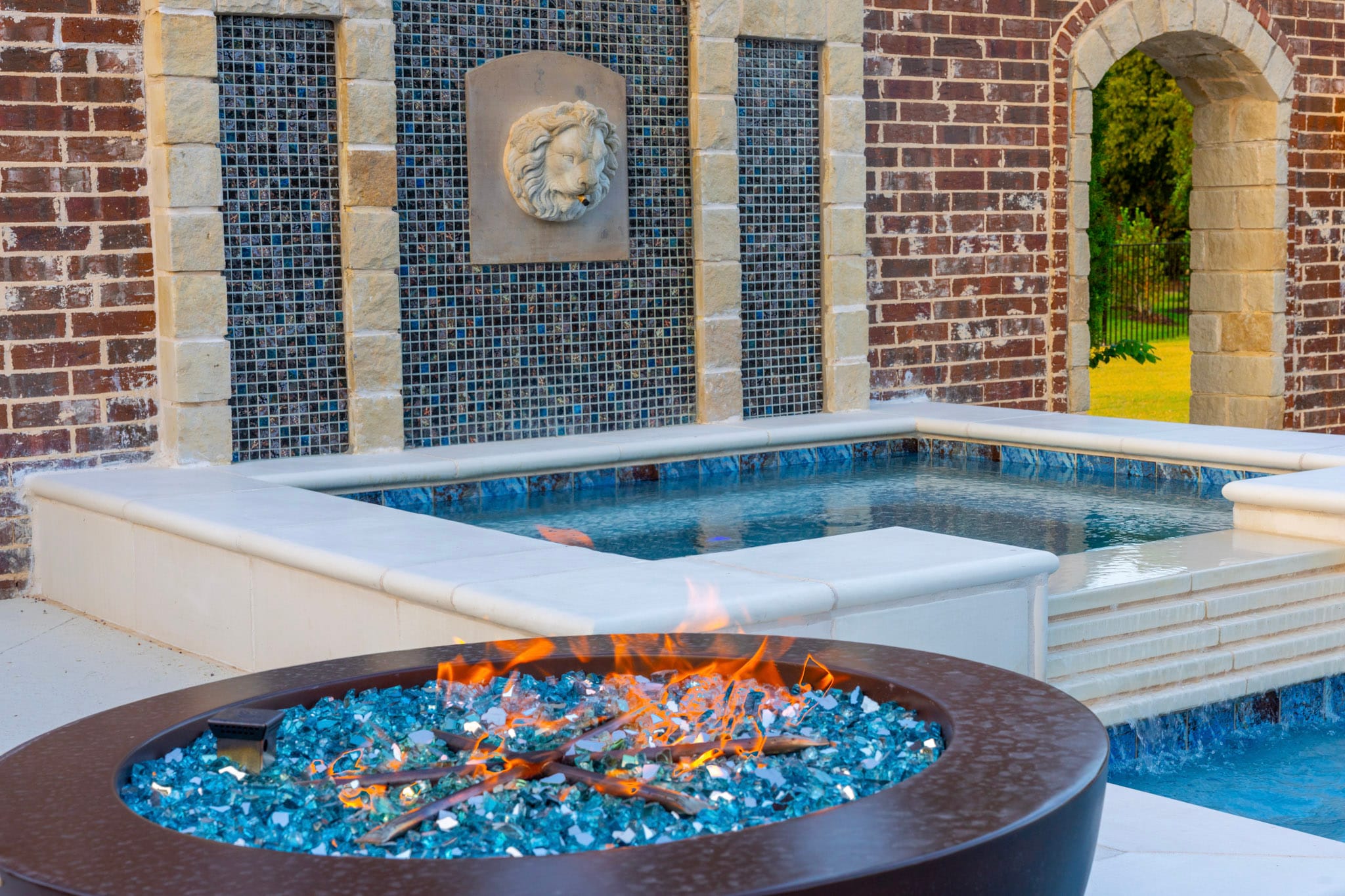Fire bowl with blue glass beside raised spa and brick wall