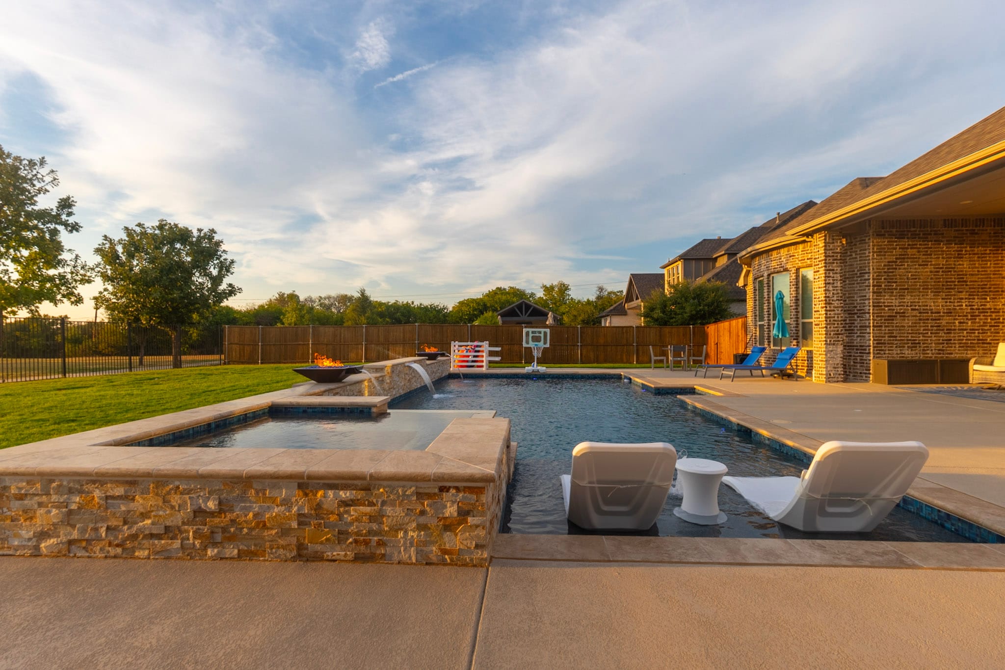 Pool with spa, in-water loungers, fire bowls, and sunset sky