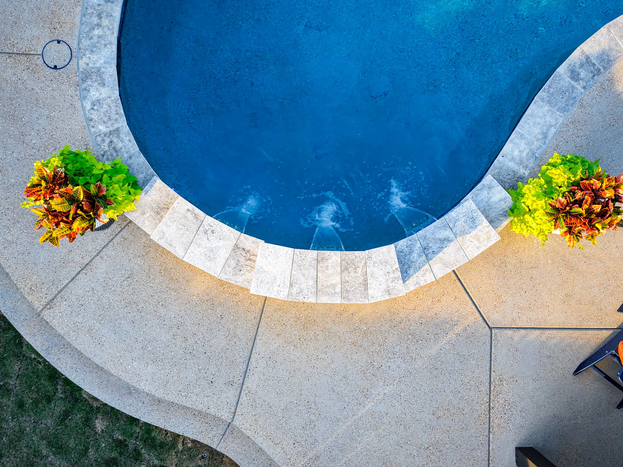 Overhead drone view of curved pool edge with three water features and planters