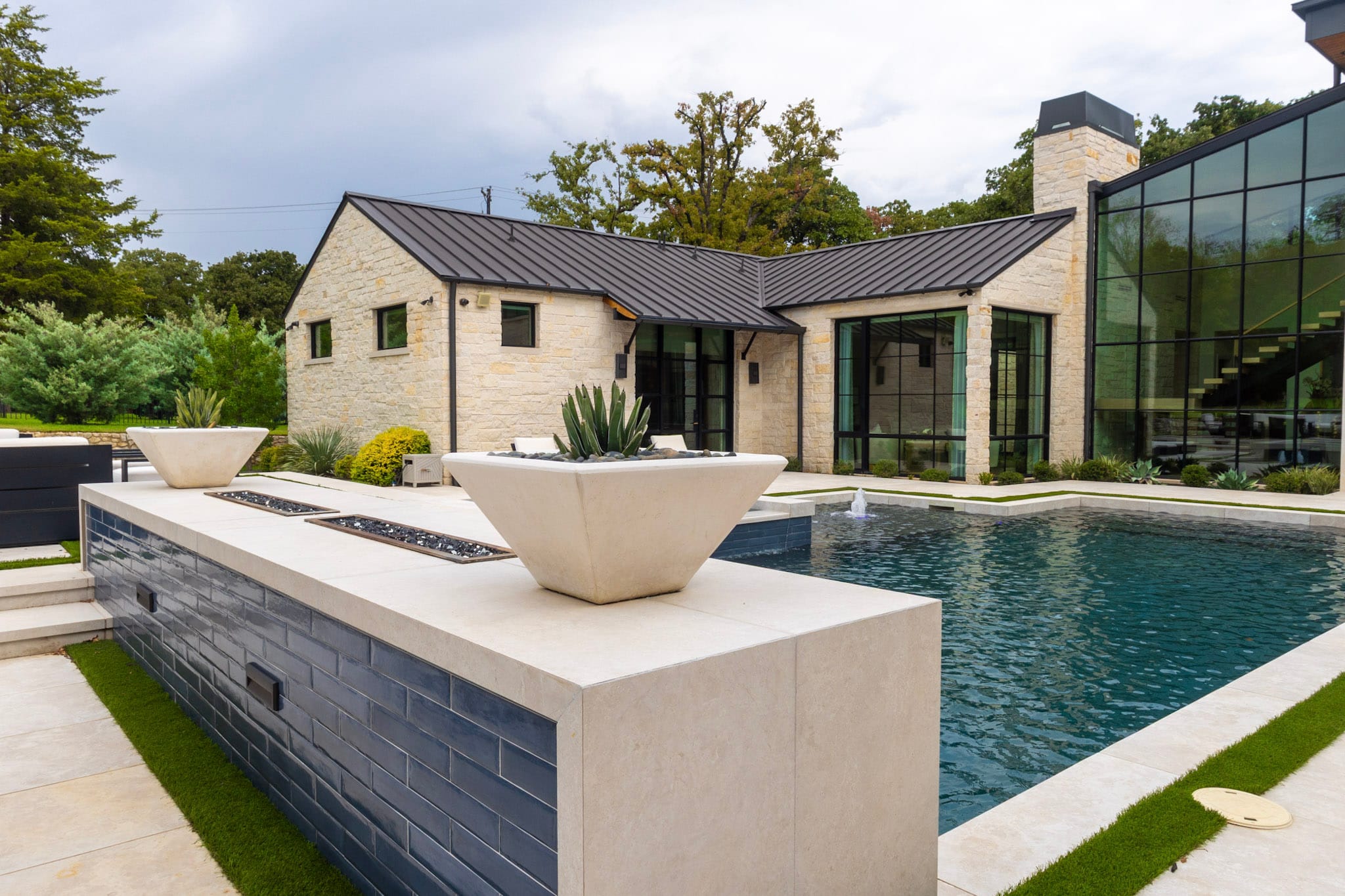 Pool beside raised blue-tile wall with planters and stone home