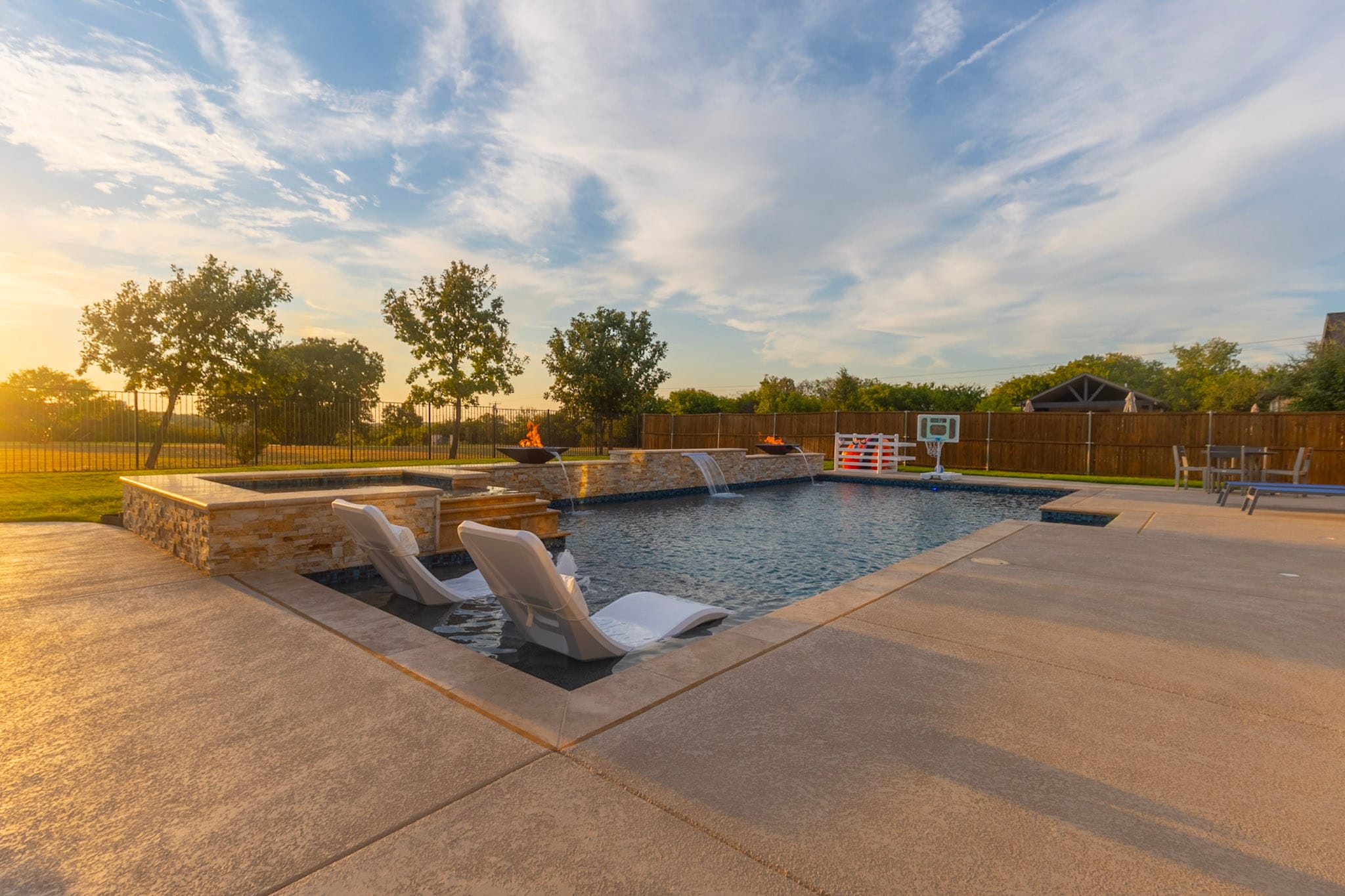 Wide pool view with in-water loungers, fire bowls, and sheer descent