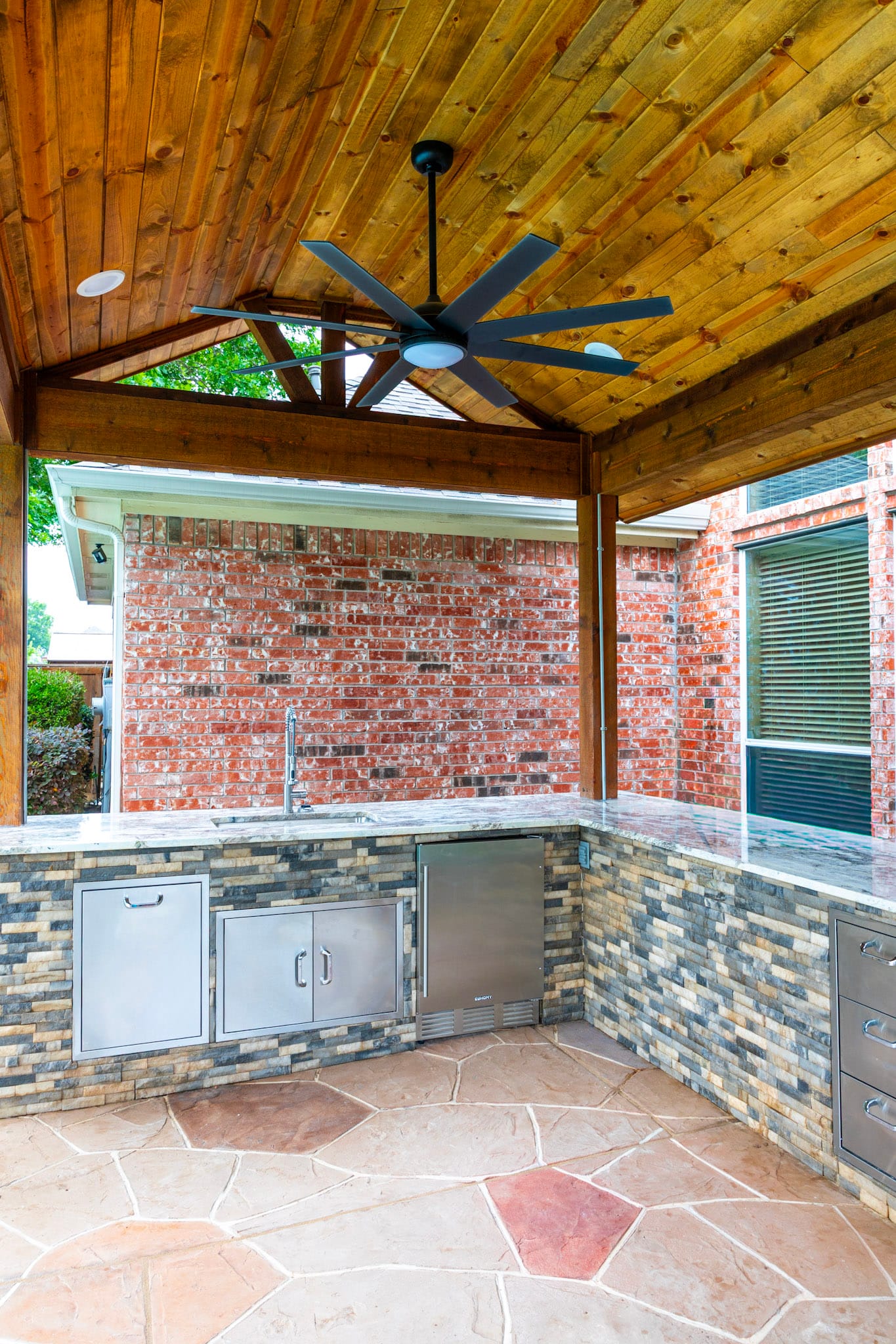 Outdoor kitchen beneath a wood ceiling with a black fan