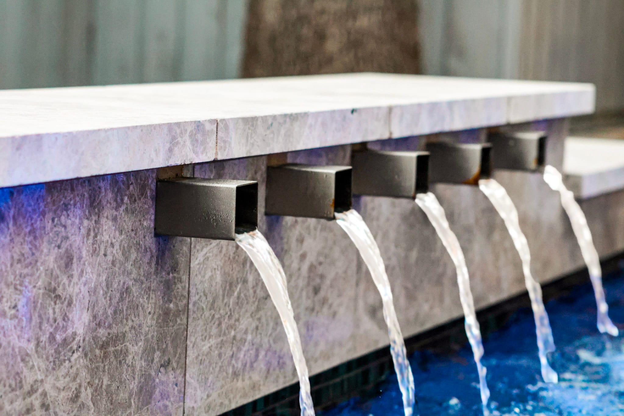 Close-up of five square water scuppers above blue pool lighting