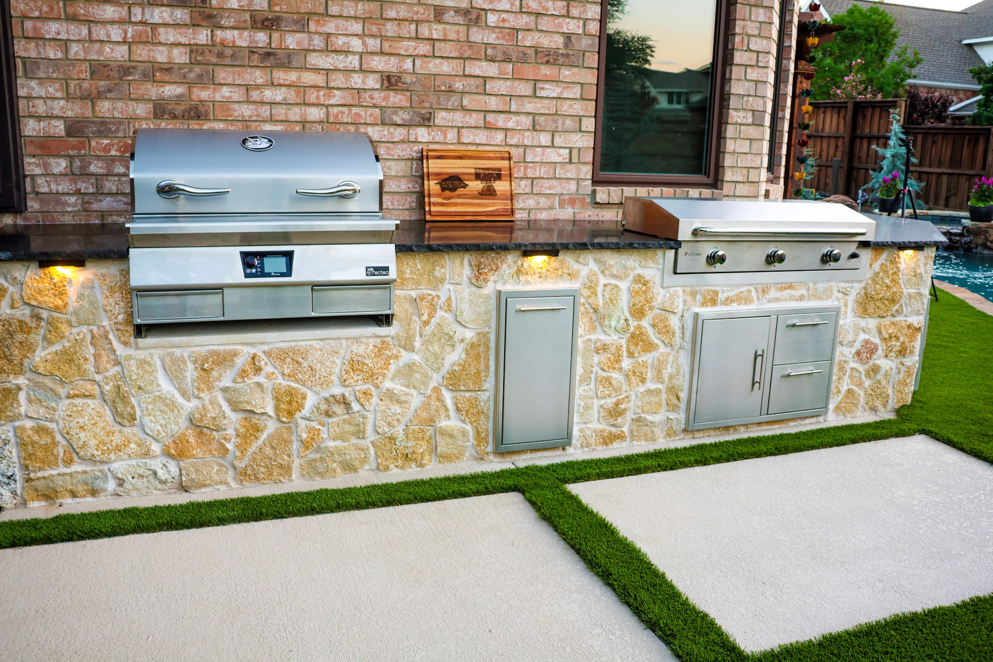 Outdoor kitchen with built-in stainless appliances beside remodeled Coppell pool