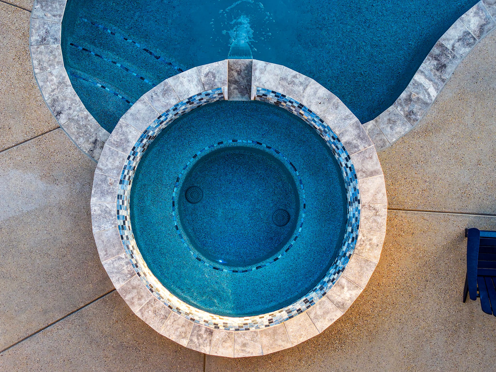 Overhead drone photograph of circular raised spa connected to a swimming pool