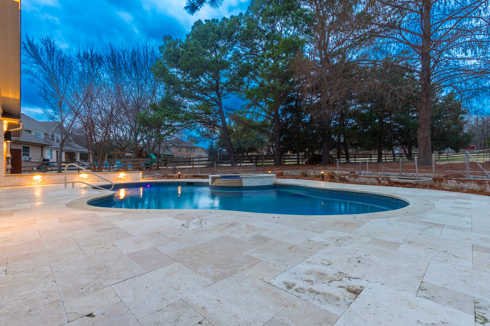 Remodeled backyard pool and travertine deck during twilight