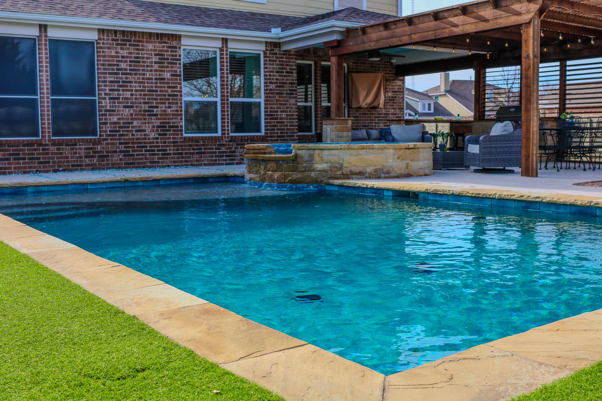 Swimming pool beside covered patio and artificial turf in Northlake Texas