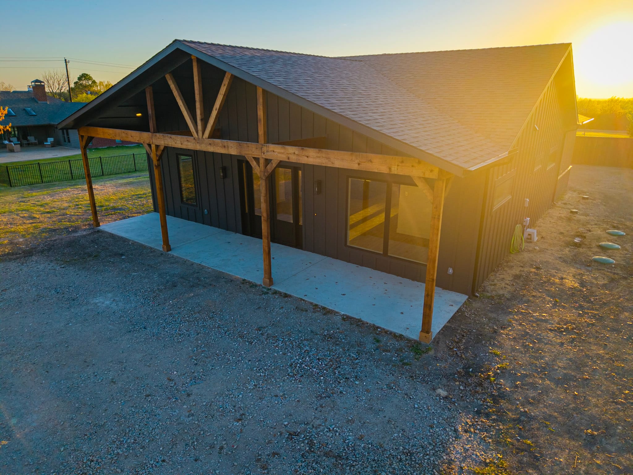 Aerial sunset view of dark barndominium with timber-framed porch