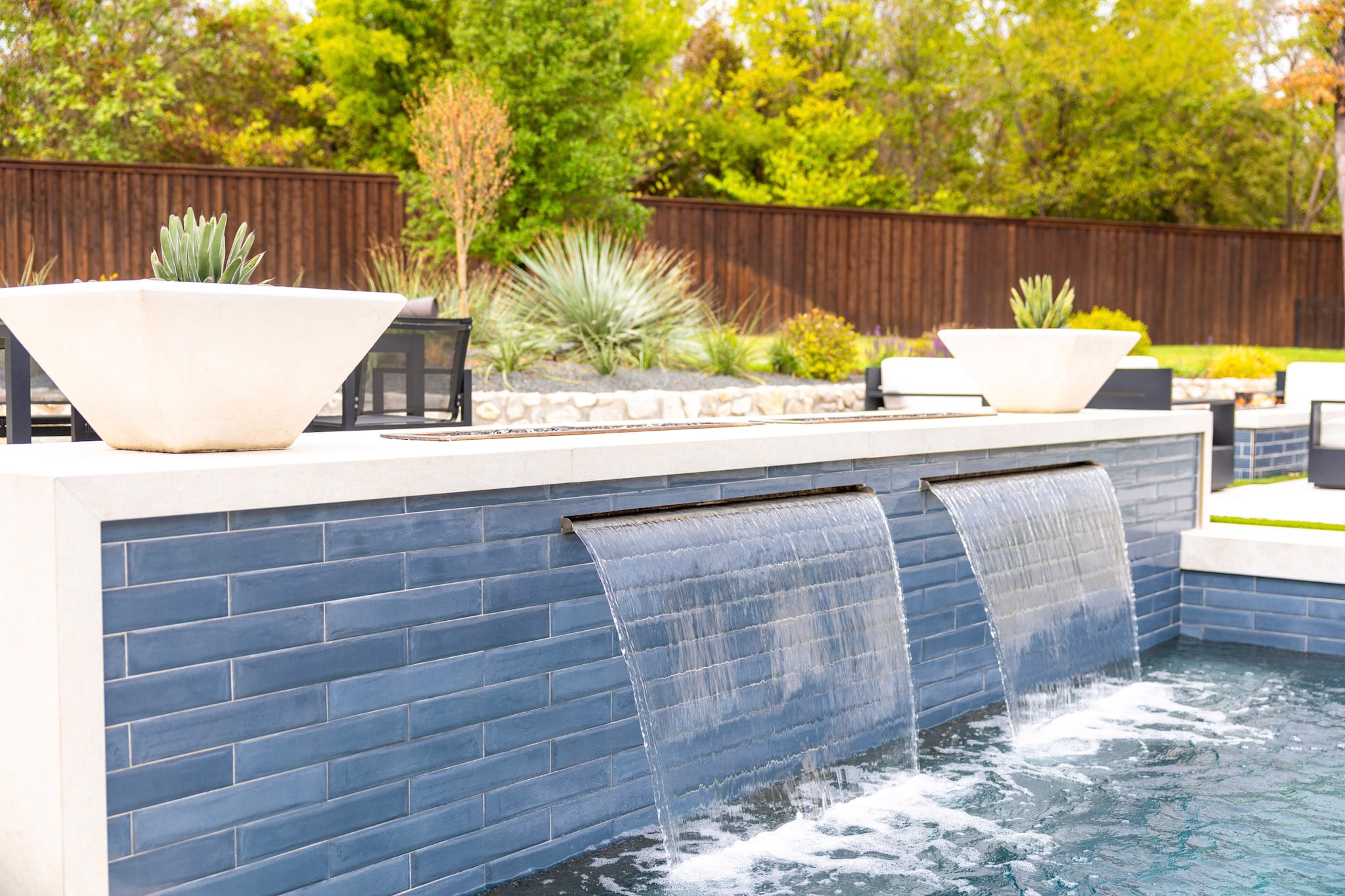 Two sheet waterfalls flowing from blue-tile wall into swimming pool