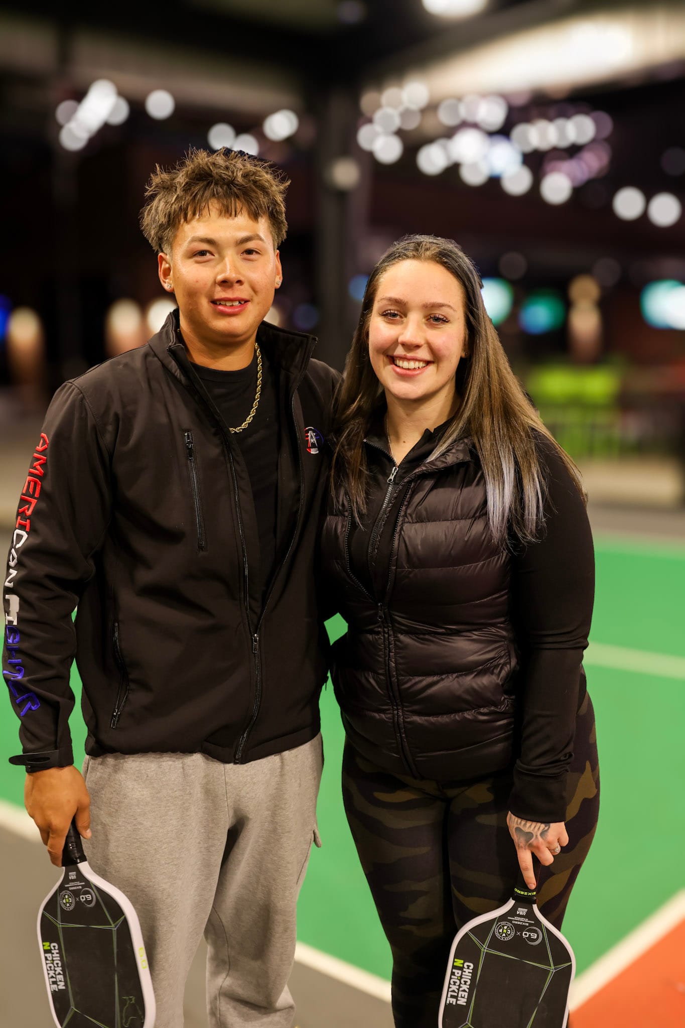 Two event attendees holding pickleball paddles on an indoor court