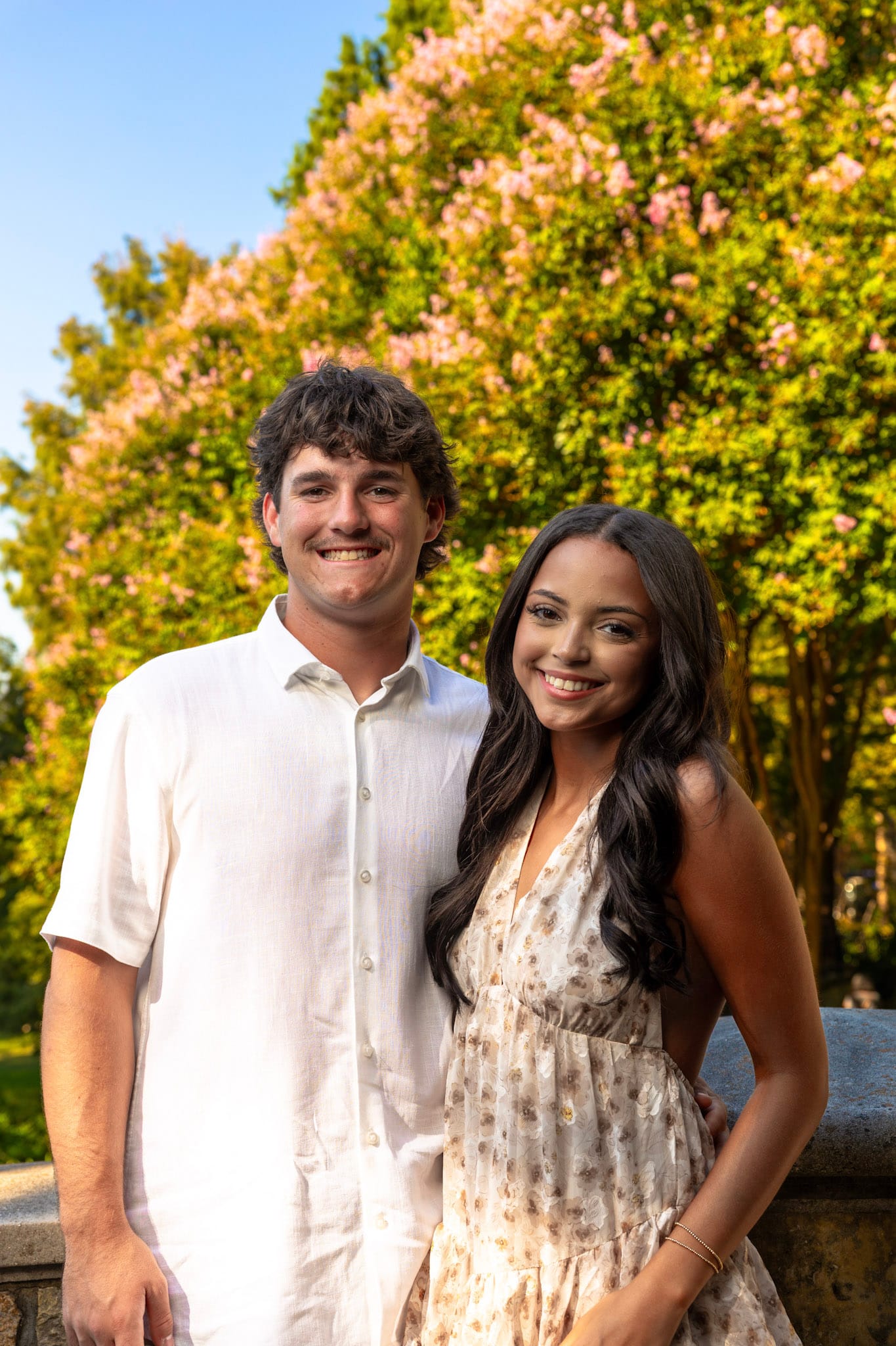 Engaged couple standing together in front of pink flowering trees