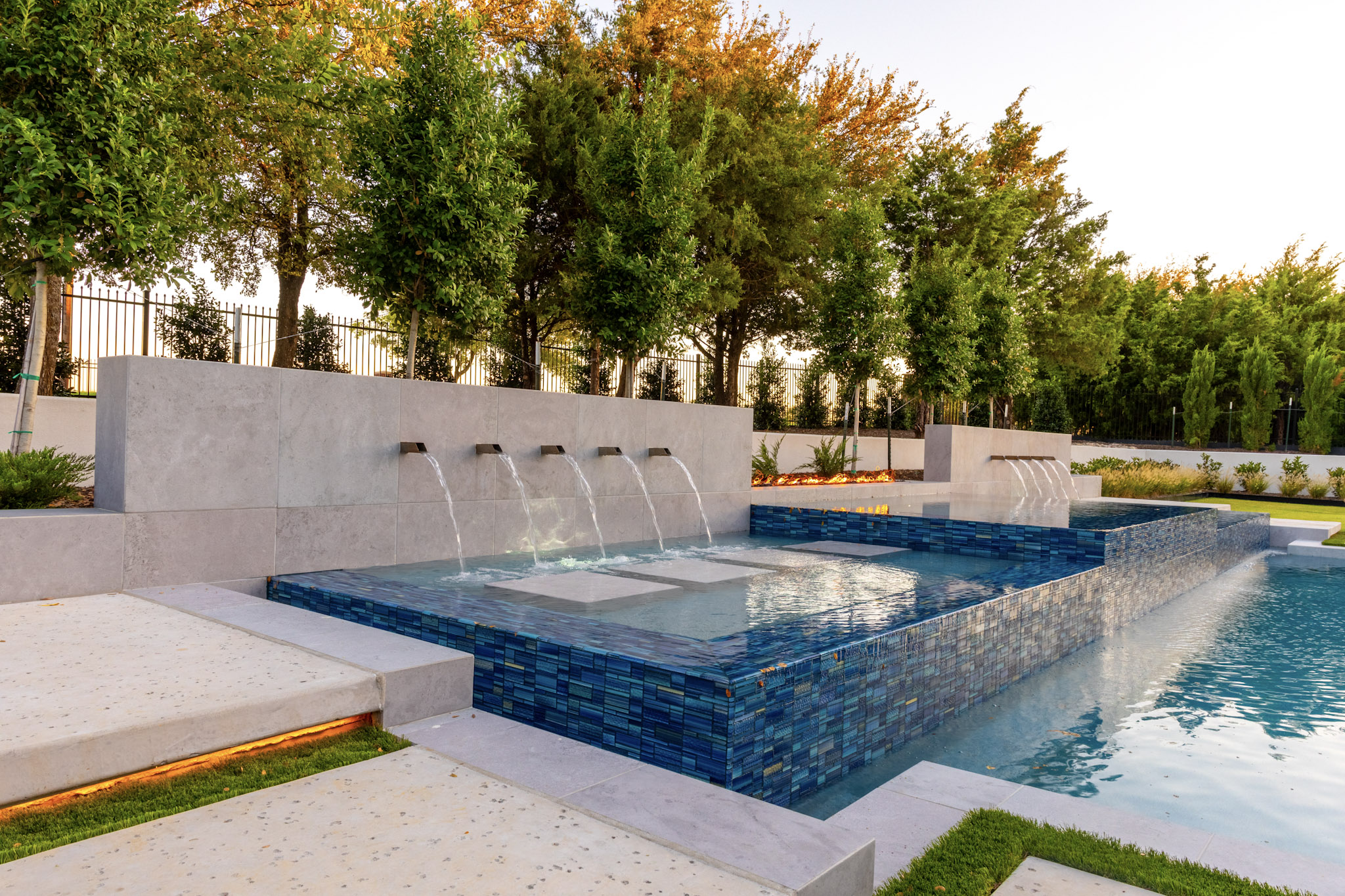 Raised blue-tiled spa beside shallow water feature and scupper wall