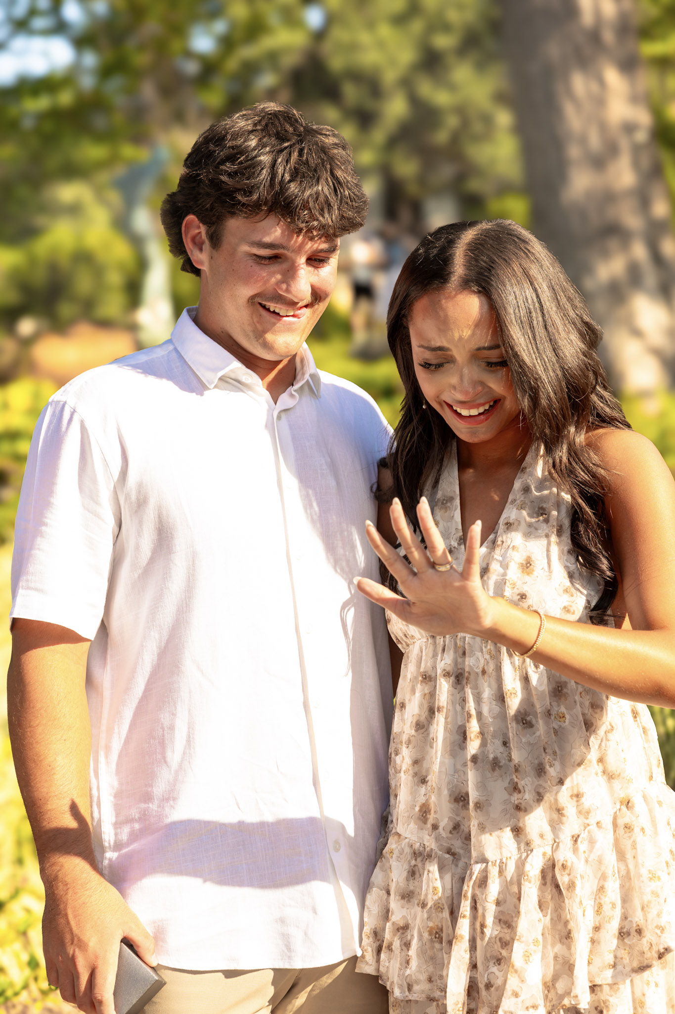 Newly engaged couple smiling while looking down at the engagement ring