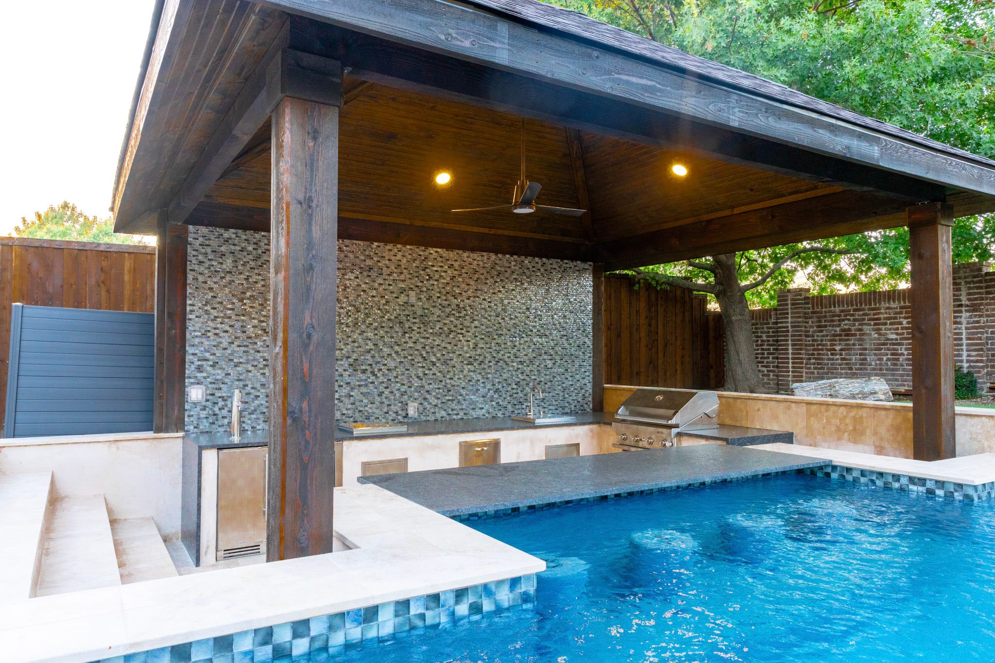 Covered sunken outdoor kitchen with grill sink and mosaic backsplash