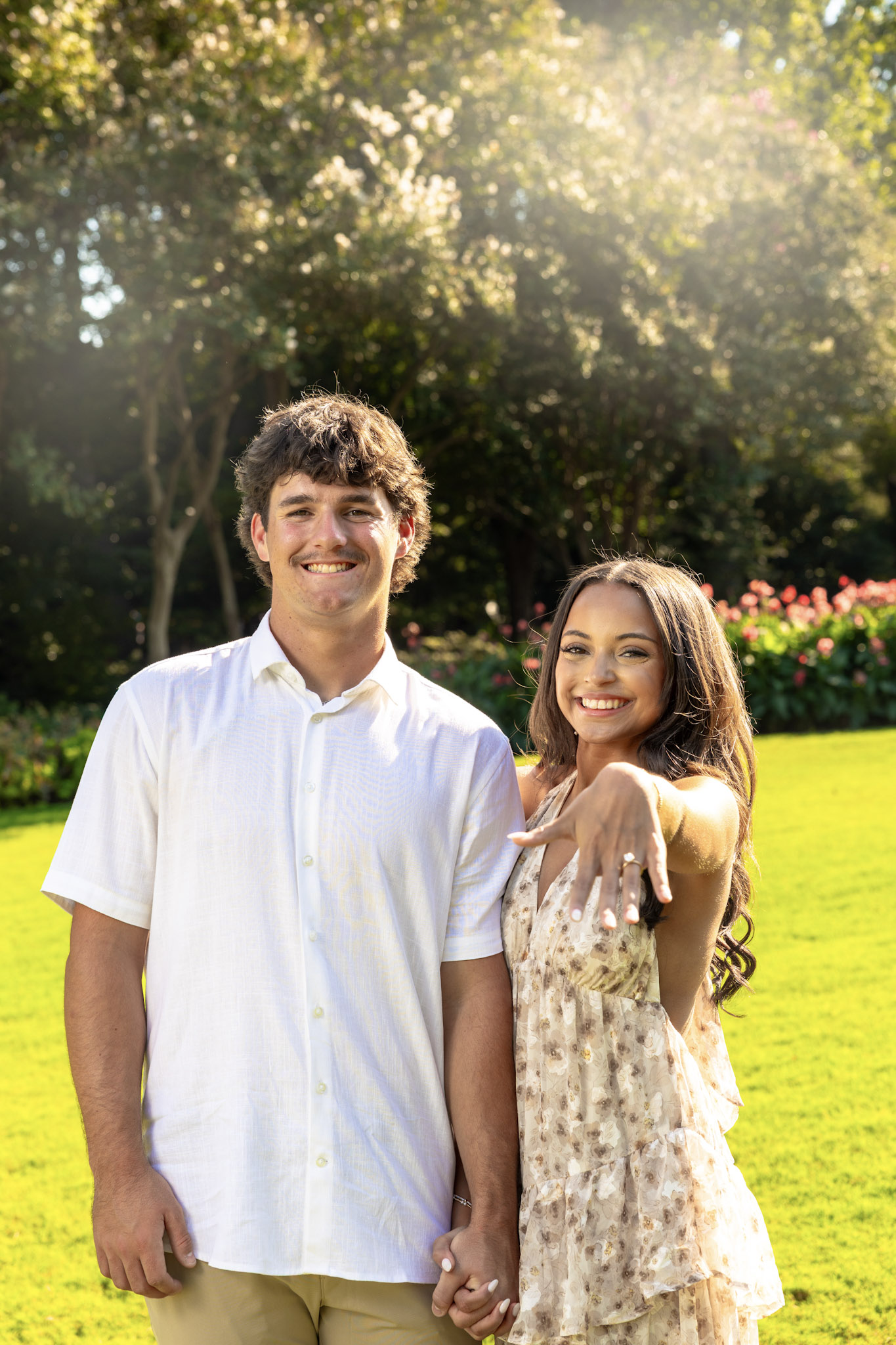 Smiling couple posing while the woman extends her engagement ring toward the camera