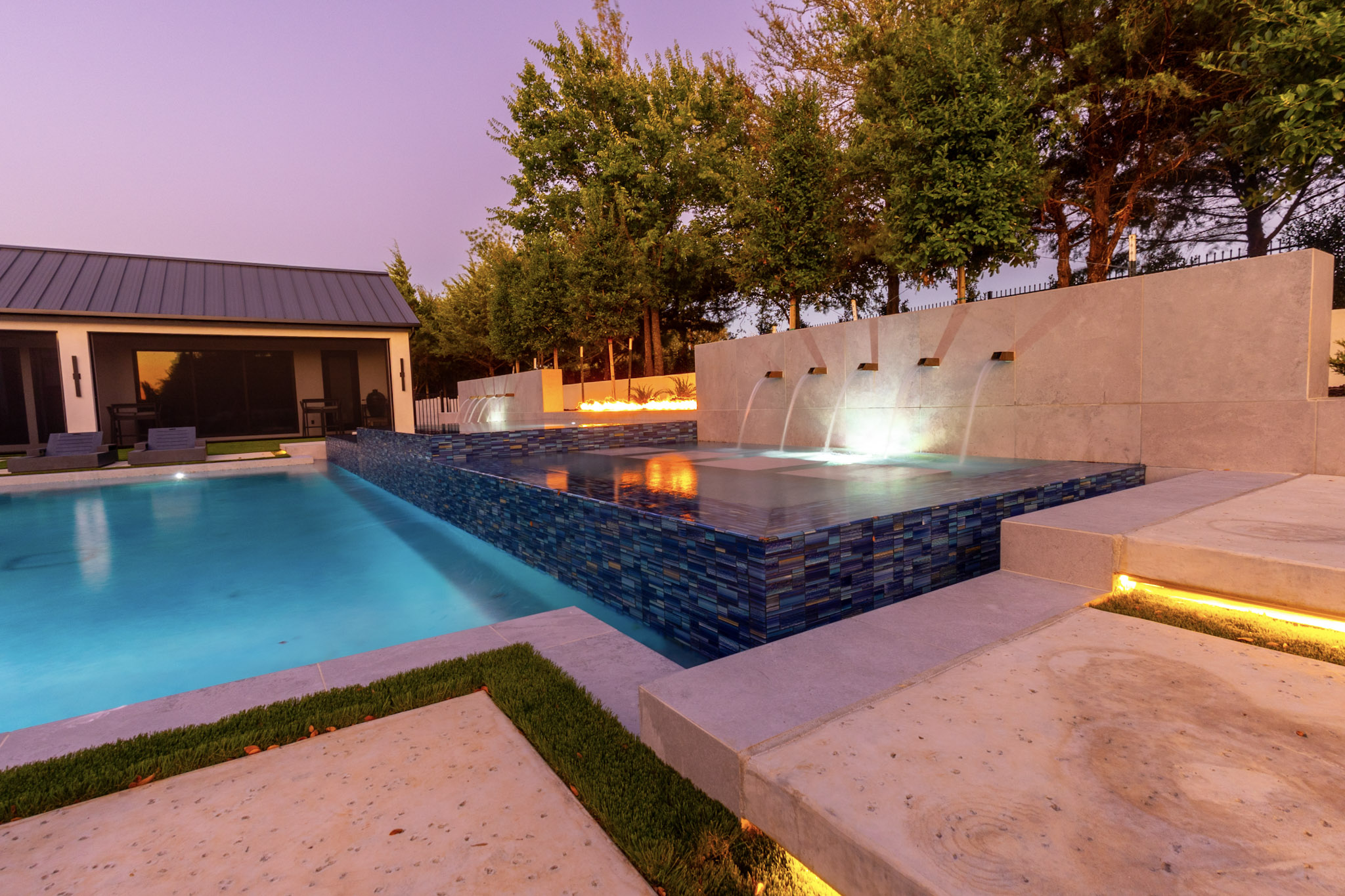 Twilight pool with raised tiled spa, illuminated scuppers, and linear fire feature